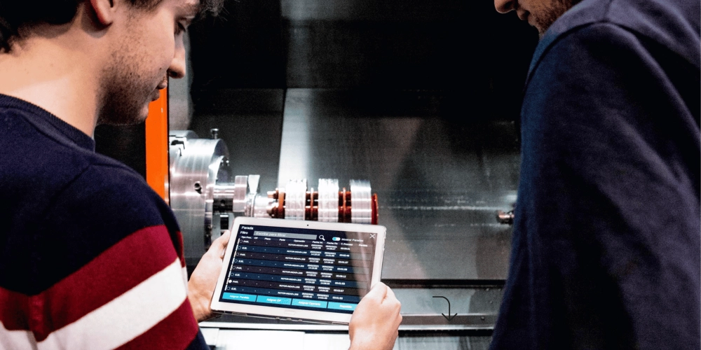 Operario industrial consultando software de gestión de taller en tablet junto a maquinaria CNC – soluciones digitales ZITU para la industria