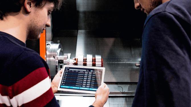 Operario industrial consultando software de gestión de taller en tablet junto a maquinaria CNC – soluciones digitales ZITU para la industria